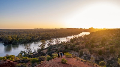 Overhead shot of three people standing on the red cliffs of the River Murray at sunset, overlooking the river bend.